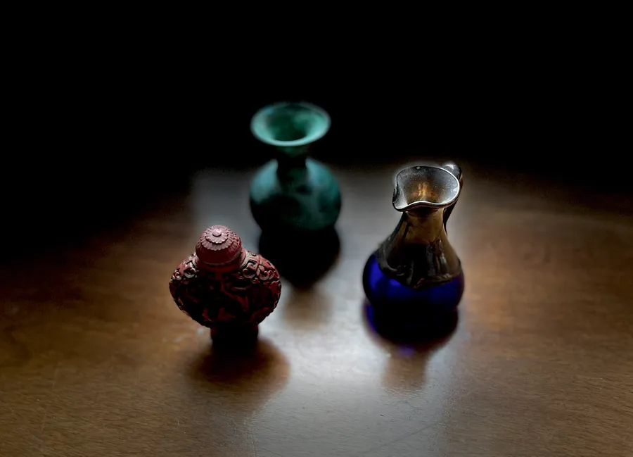 Three small vessels in green, red and blue glass lit on a dark table, photograph by Esther Piaskowski
